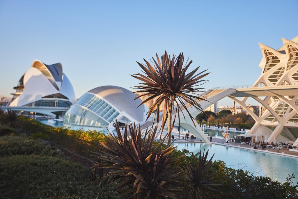 Cité des Arts et des Sciences à Valence avec bâtiments modernes, bassin d’eau et palmiers sous un ciel bleu.