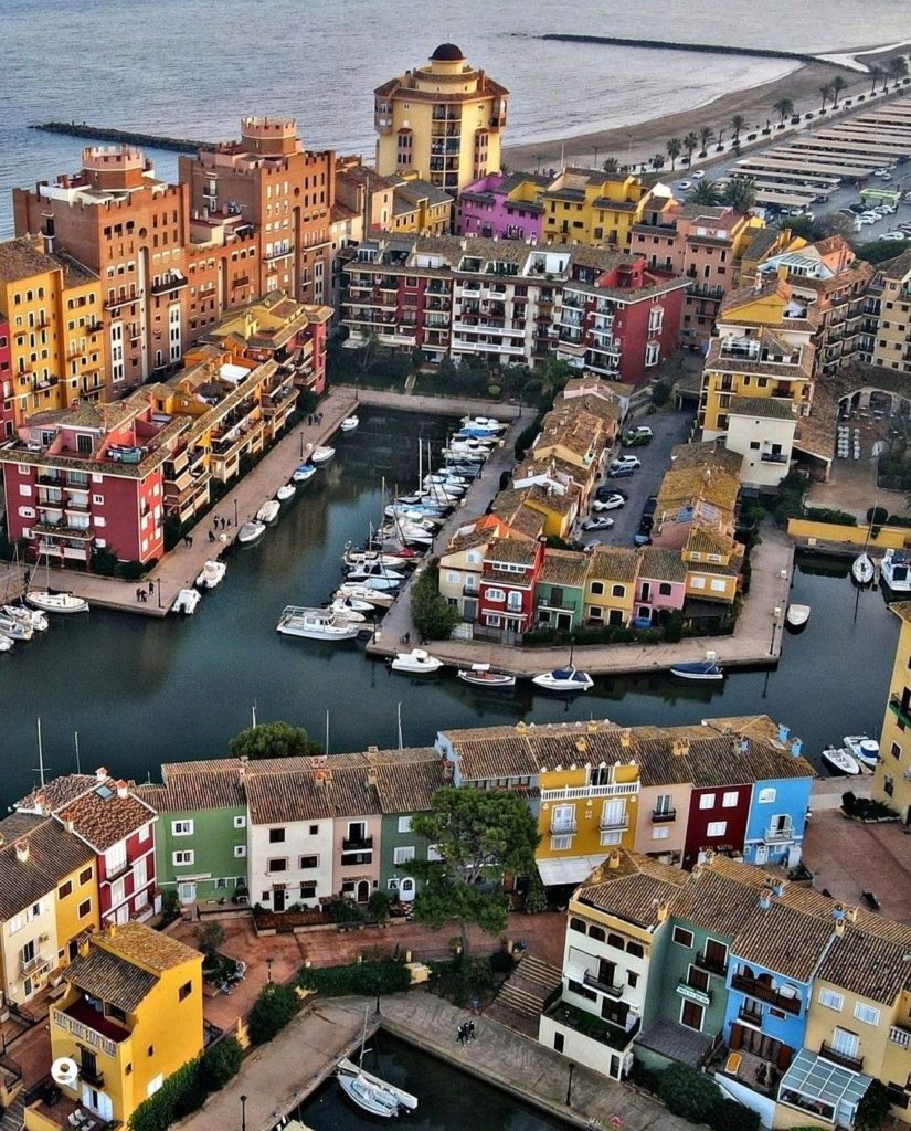 Vue aérienne d’un quartier résidentiel coloré en bord de mer en Espagne avec port et bateaux, idéal pour une retraite au soleil