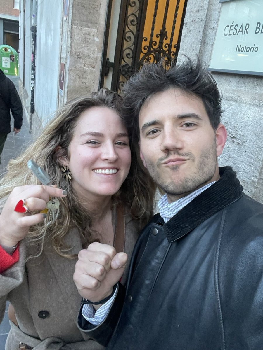 Deux clients souriants brandissent les clés de leur appartement devant la porte d'une étude notariale.