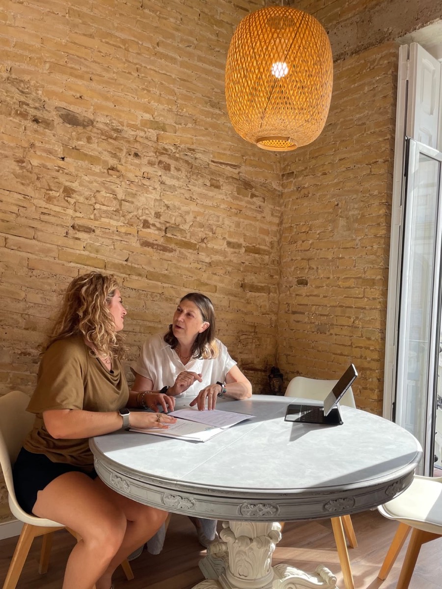 Deux personnes travaillent sur un dossier autour d'une table, dans le bureau de l'agence aux murs de brique.